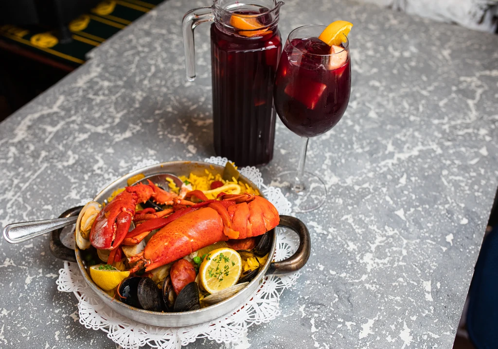 Close-up of Spanish seafood paella with lobster, sangria, and lemons.