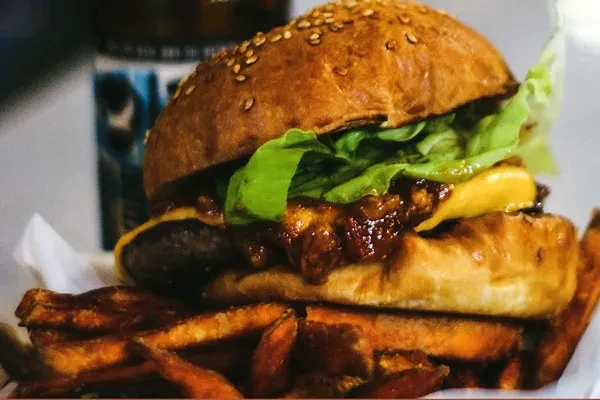 Gourmet burger with melted cheese, sauce, lettuce, and sweet potato fries.