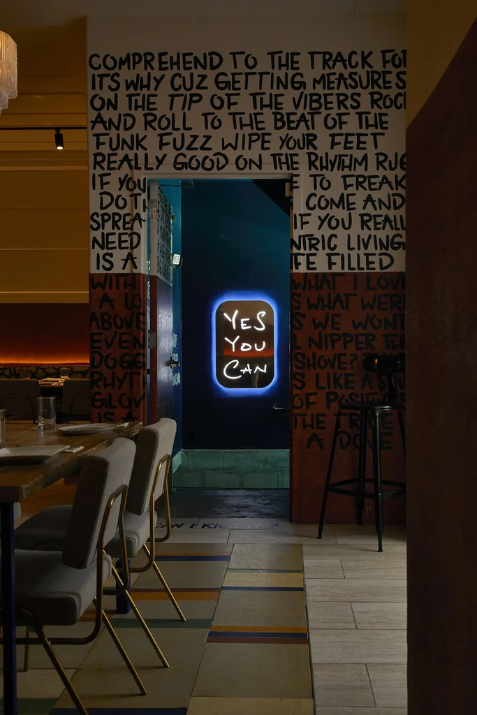 Restaurant interior with handwritten text walls and a 'YES YOU CAN' neon sign.