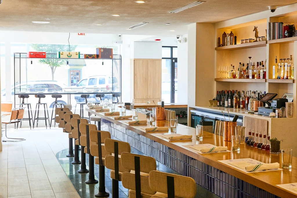 Bright, modern bar with wooden counter, stools, and street view.