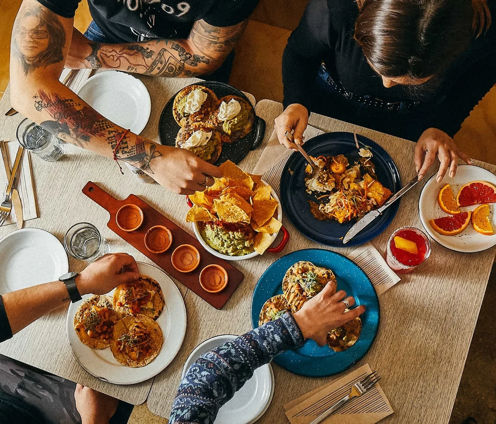 Overhead view: wooden table laden with food, drinks, and hands eating.
