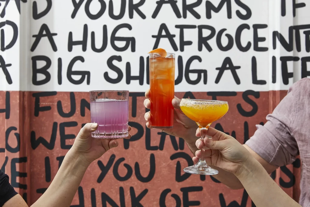 Three colorful drinks held by hands against a graffiti wall.