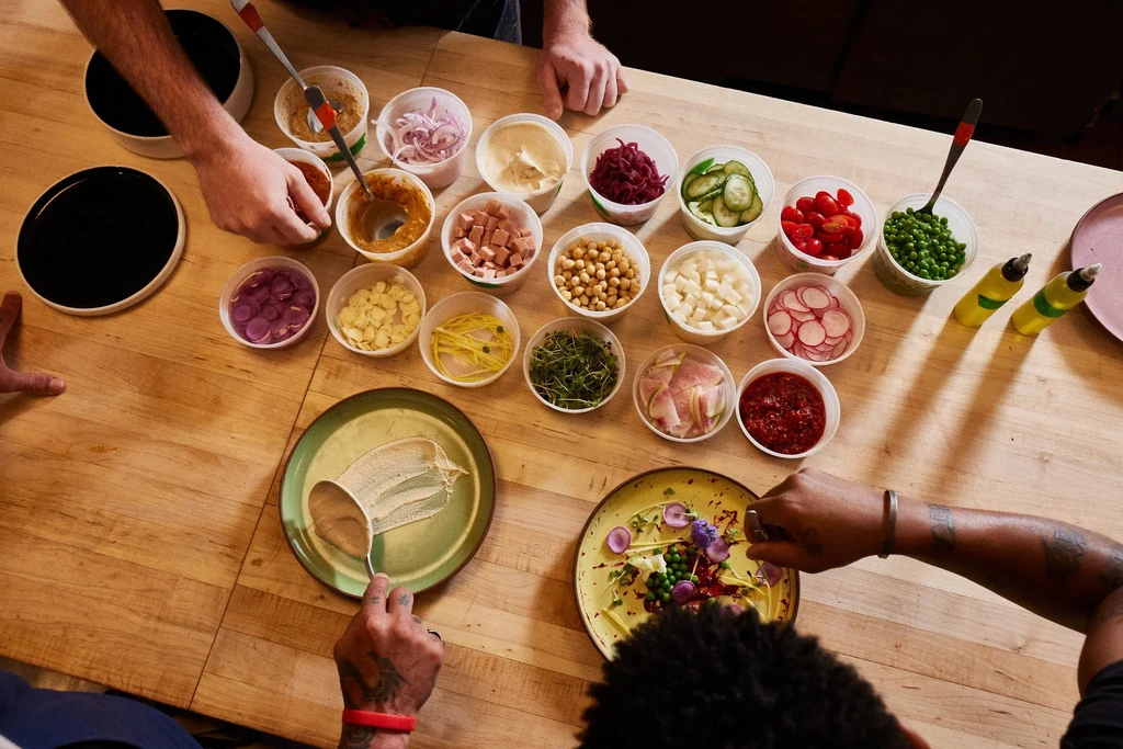 High-angle view of hands plating diverse ingredients from small containers.