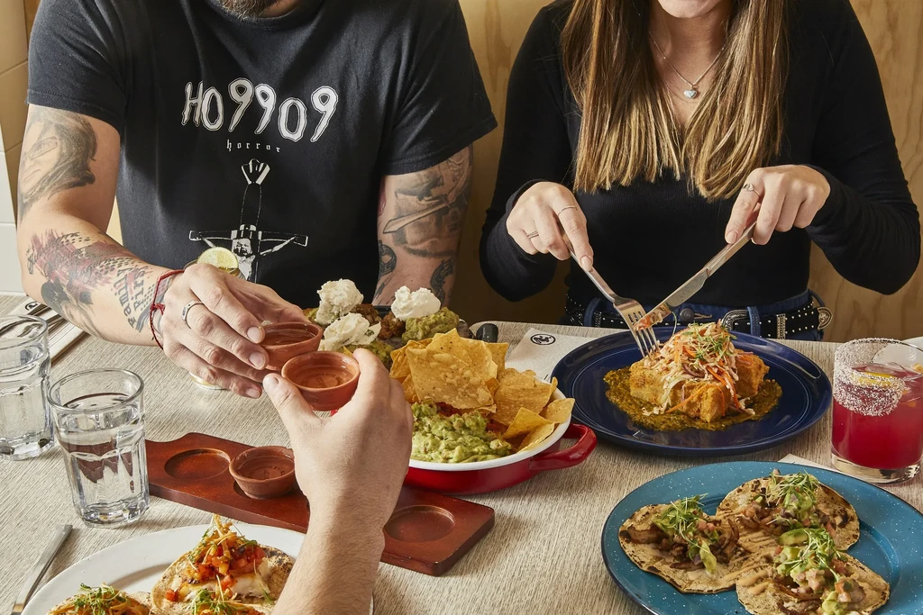 Hands sharing diverse dishes, cocktails, and water at a restaurant.