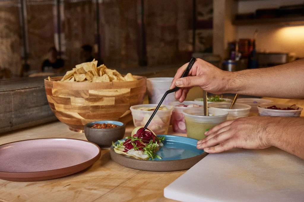 Chef's hands precisely plating fish tacos with microgreens in a kitchen.
