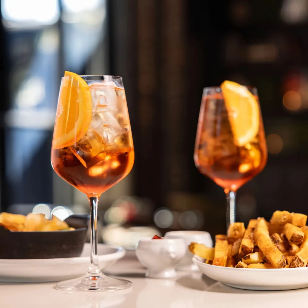 Two orange cocktails, french fries, and ketchup on a white table.