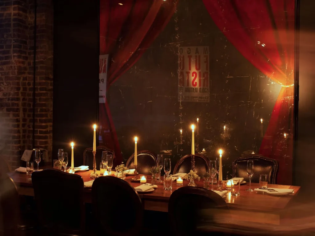 Elegant, candlelit wooden dining table set with glasses and plants.