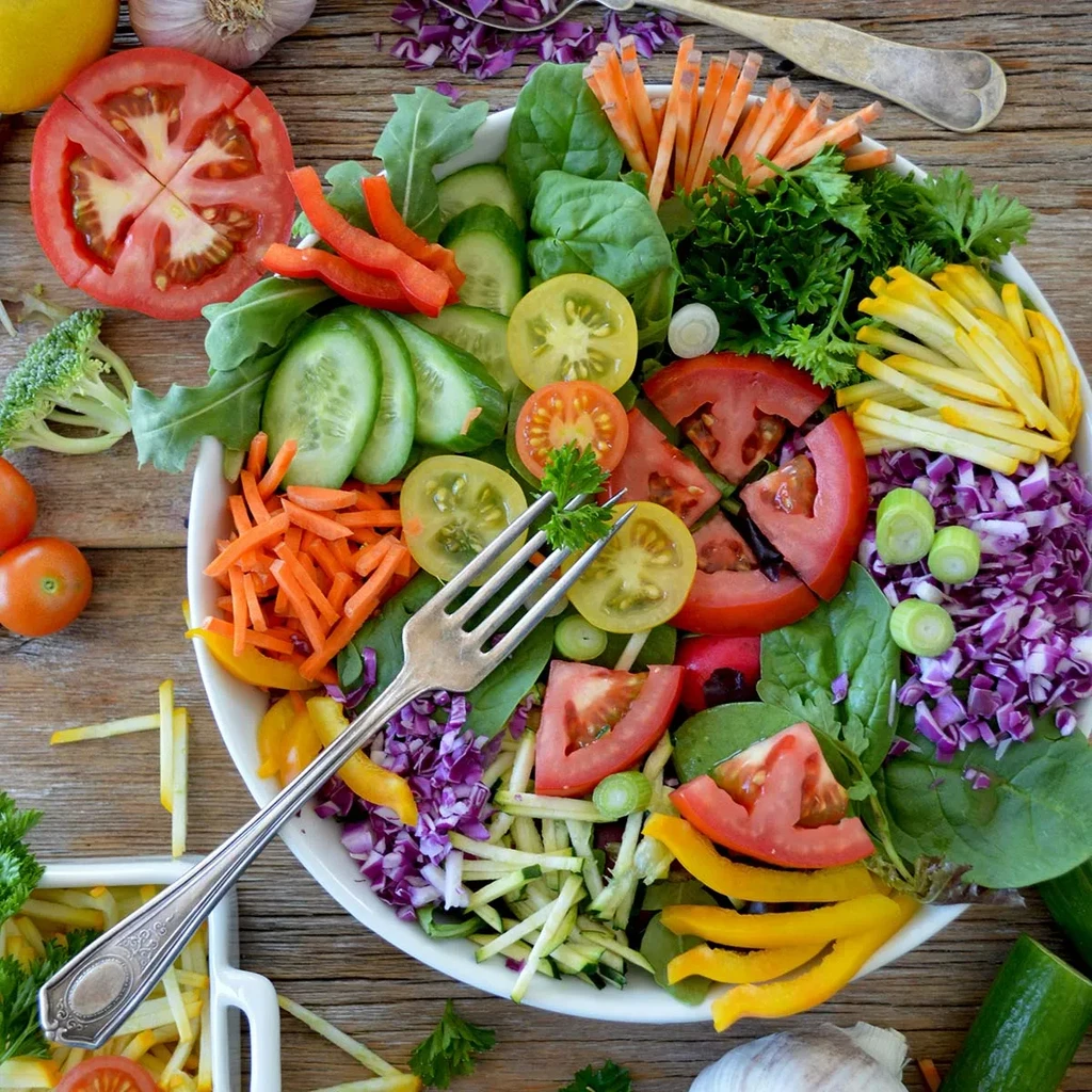 Vibrant mixed vegetable salad with fork on rustic wooden table.