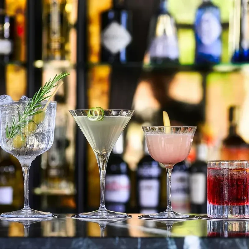 Four distinct cocktails on a bar counter with blurred liquor bottles.