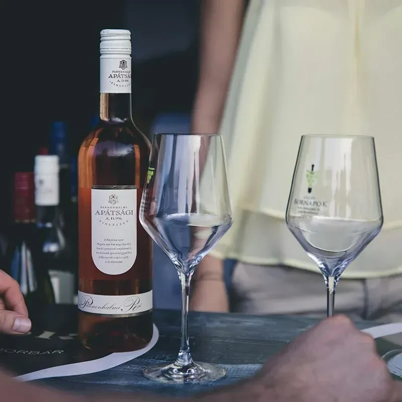 Rose wine bottle, two empty glasses, hands on a rustic wooden table.
