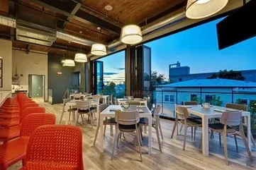 Empty modern restaurant with red bar stools, open doors to evening sky.