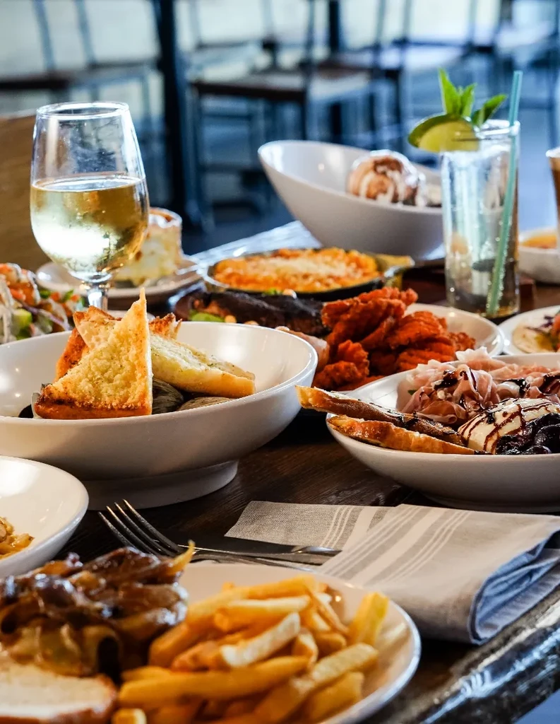 Restaurant table with wine, cocktails, charcuterie, and various food dishes.
