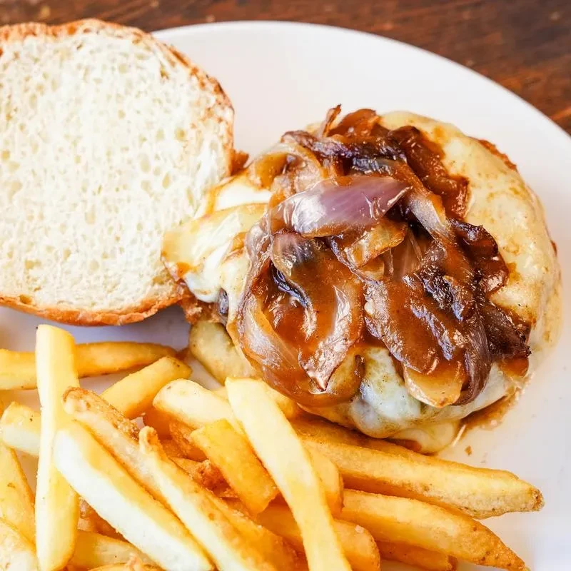 Close-up of gourmet burger with melted cheese, caramelized onions, and fries.
