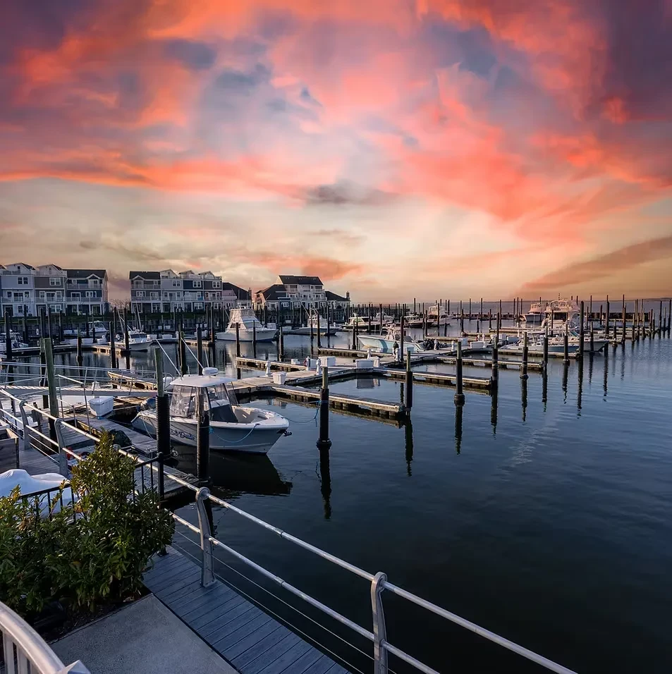 Boats docked at a marina under a vibrant sunrise or sunset sky.