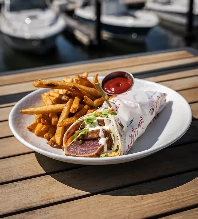 Seared tuna wrap and french fries served on a waterfront deck.