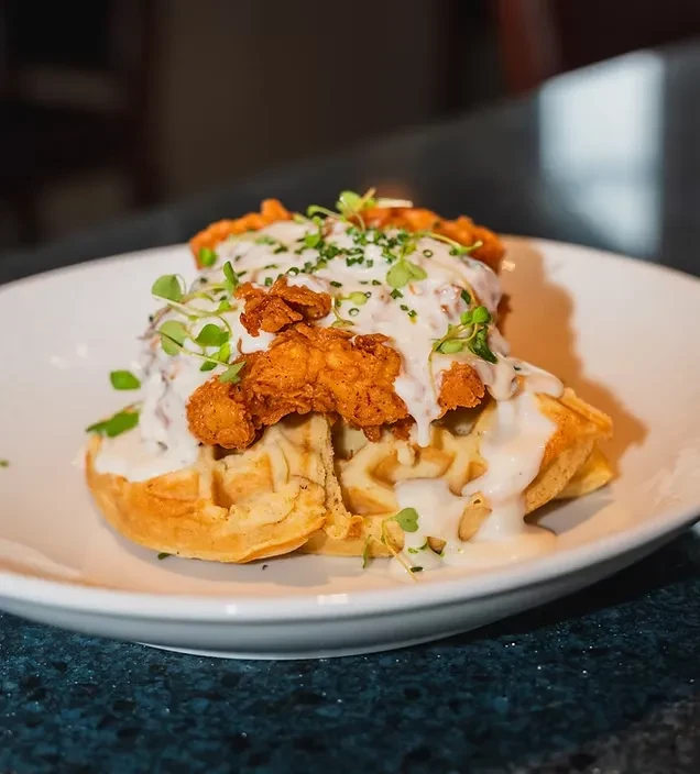 Golden-brown, crispy chicken and waffles with creamy sauce and herbs.