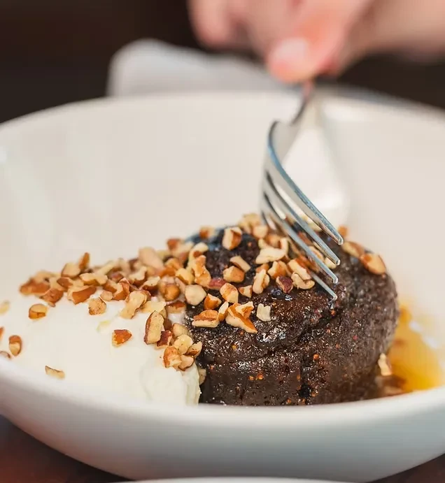 Dark dessert with nuts, cream, and a fork in a white bowl.