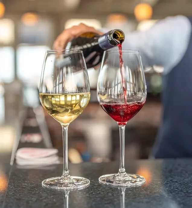 Red wine pours into a glass, beside a glass of white wine.