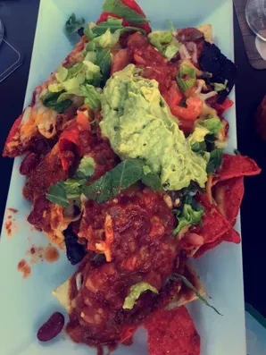 A plate of nachos topped with guacamole, salsa, and beans.