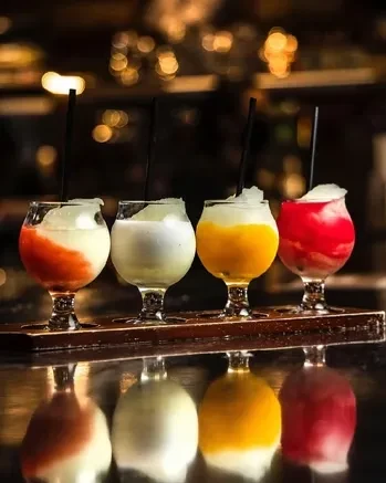 Four colorful frozen drinks in clear glasses on a dark wooden tray.
