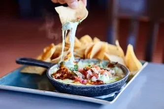 Hand dips chip into steaming queso dip with pico de gallo.