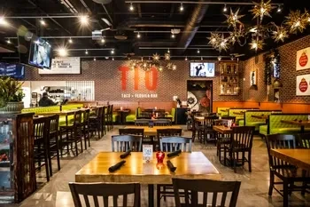 Modern industrial-chic restaurant interior with lime-green booths and a "110 TACO" sign.