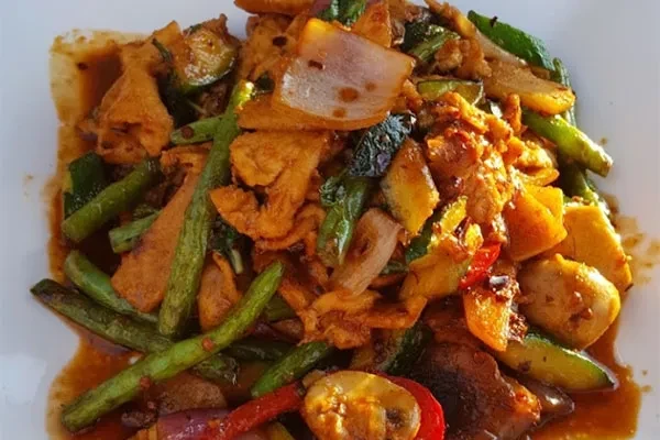 A plate of cooked chicken, green beans, onions, and zucchini.