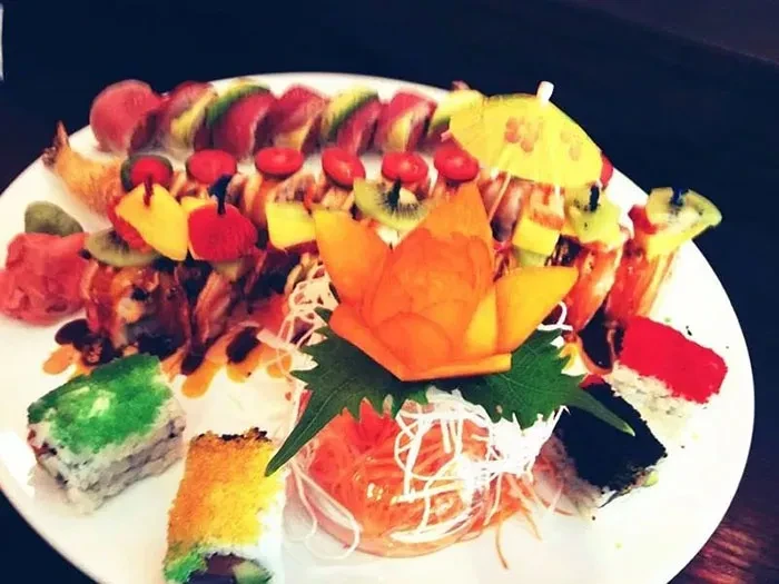 A large sushi platter with various rolls, fruit, and an umbrella.
