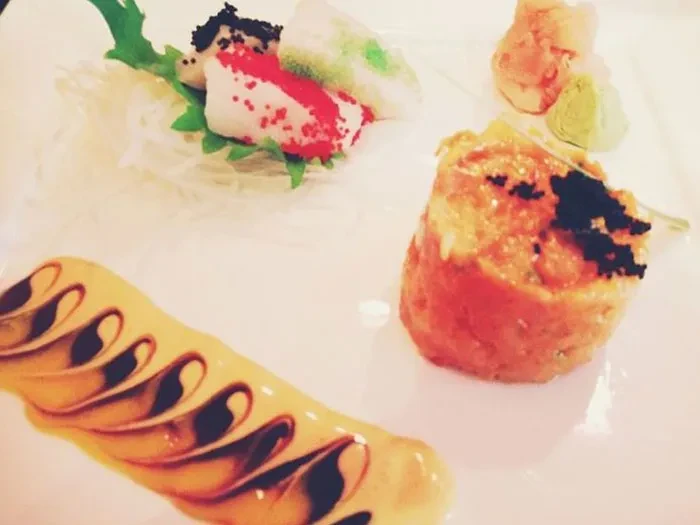 A plate of sushi with sauce swirls, roe, and garnishes.