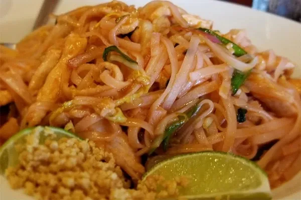 A white plate holds Pad Thai noodles with lime and peanuts.