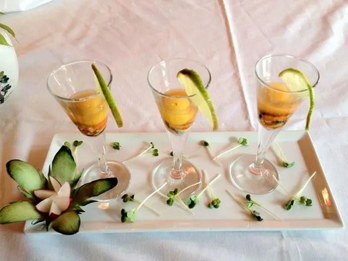 Three glasses of yellow liquid with lime garnish on a white tray.