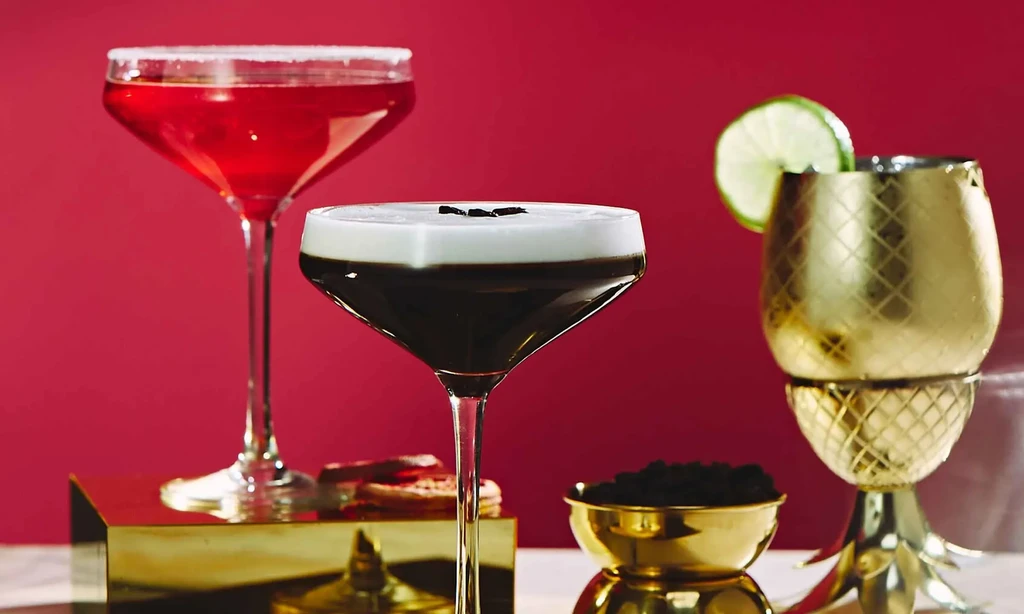 Studio still life of three cocktails with golden decor on a red background.