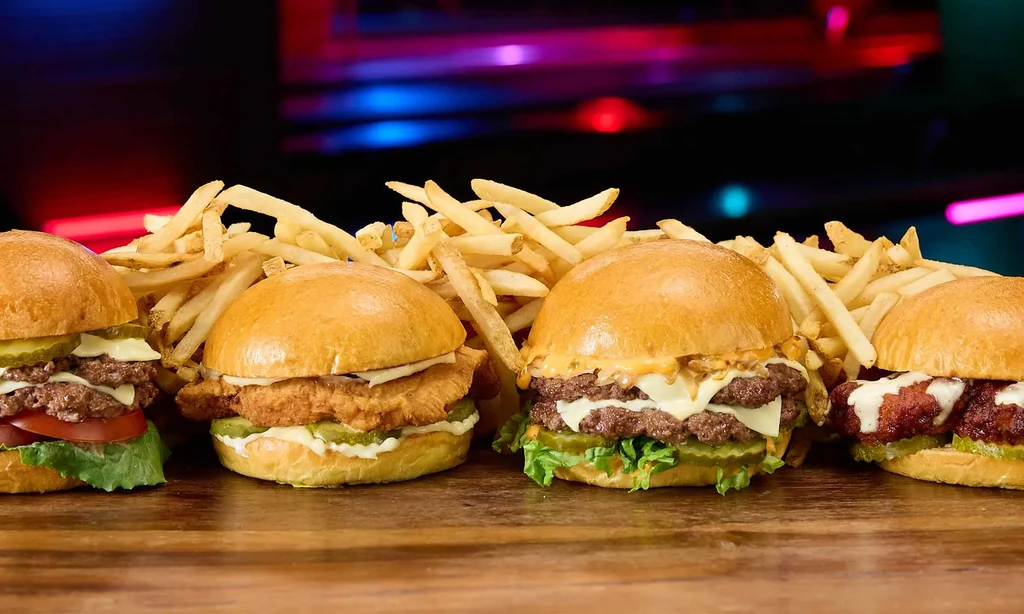Four varied burgers and fries on a wooden surface.