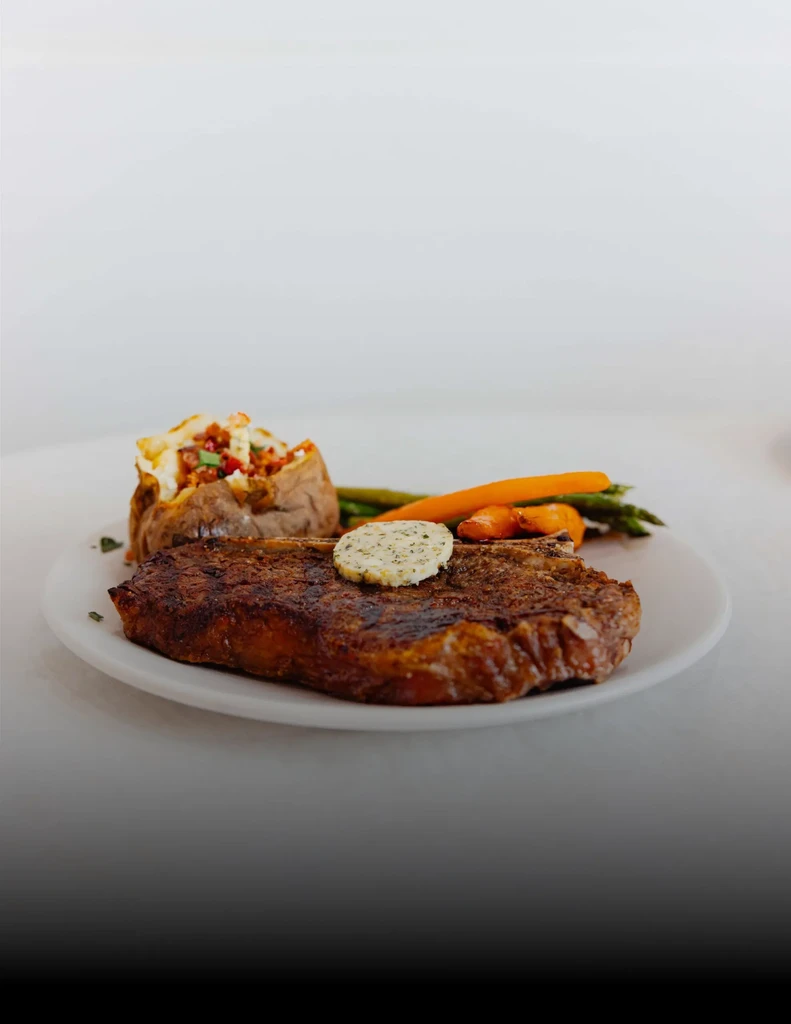 Grilled steak with butter, loaded potato, and vegetables on a white plate.