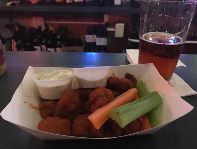 Chicken wings, celery, carrots, and dips in a paper tray with beer.