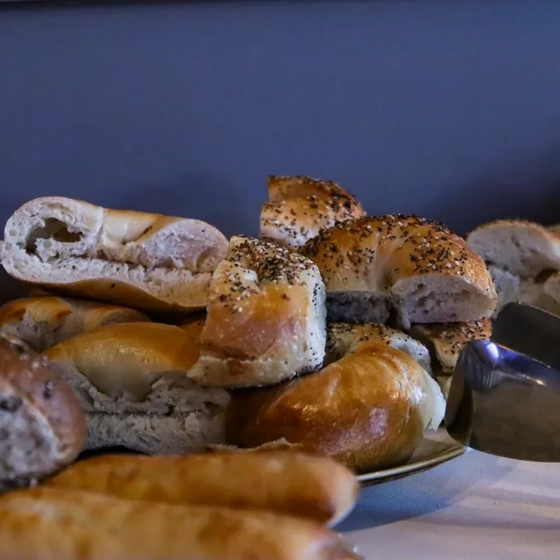Assortment of cut bagels and rolls with seeds and serving tongs.