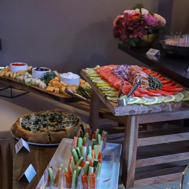 Beautifully arranged buffet with smoked salmon, vegetables, quiche, cheeses, and dips.