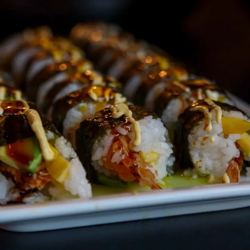 Maki sushi rolls with shrimp tempura, avocado, mango, and sauces.
