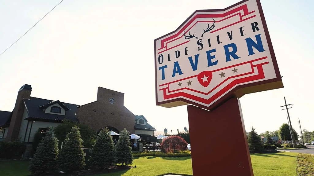 Crest-shaped Olde Silver Tavern sign with antlers and brick building.