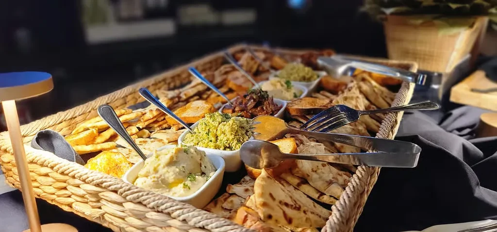 Woven basket of breads, crackers, and three dips with serving utensils.