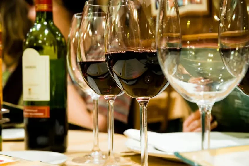 Close-up: red wine glasses, green bottle, on a blurred restaurant table.