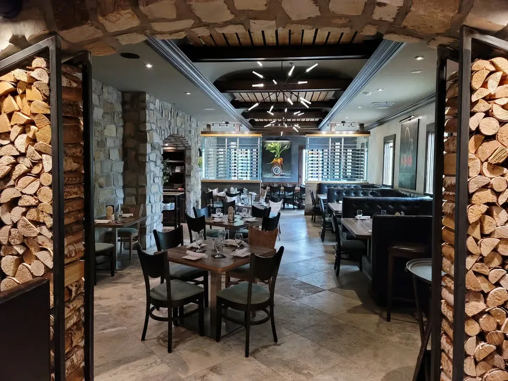 Well-lit upscale restaurant interior with stone arch, firewood, and wine display.