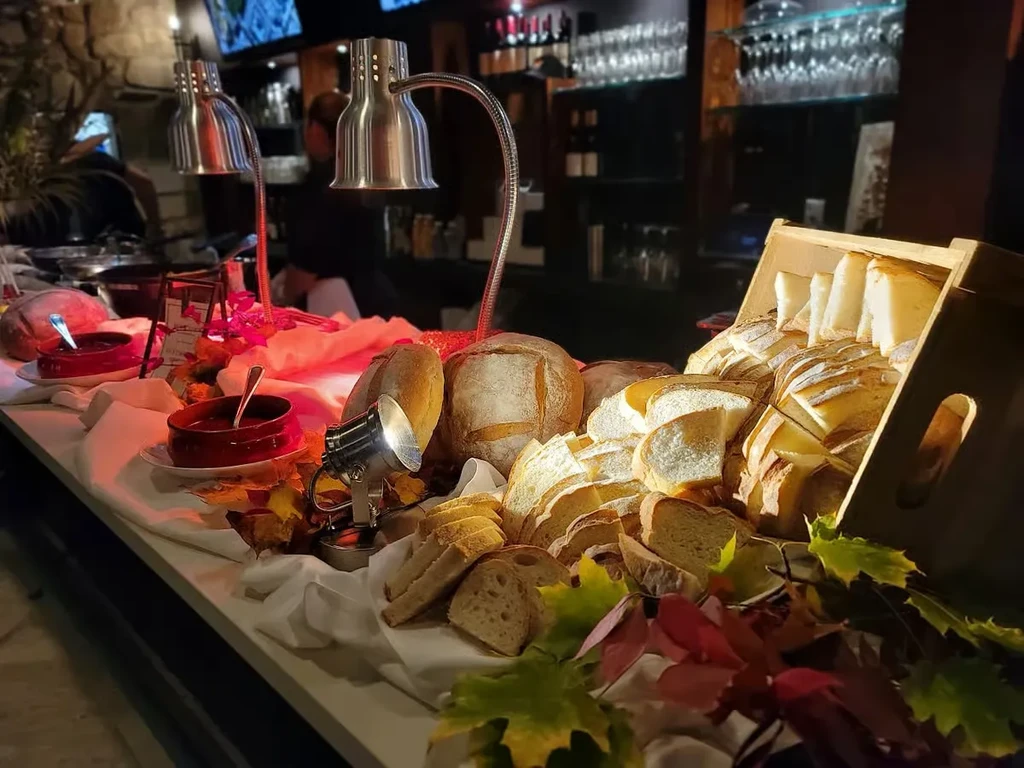 Buffet spread with breads, two hot red liquid bowls, and autumn leaves.