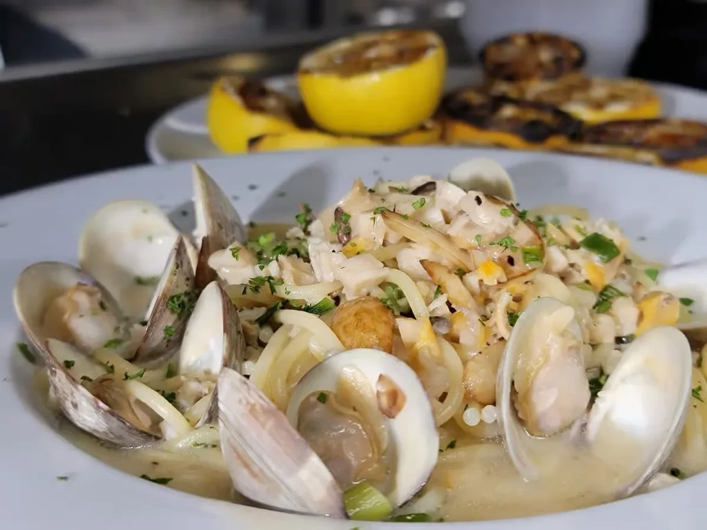 White bowl of creamy clam pasta garnished with fresh green herbs.