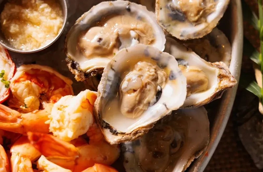 Close-up seafood platter with fresh oysters, cooked shrimp, and dipping sauce.