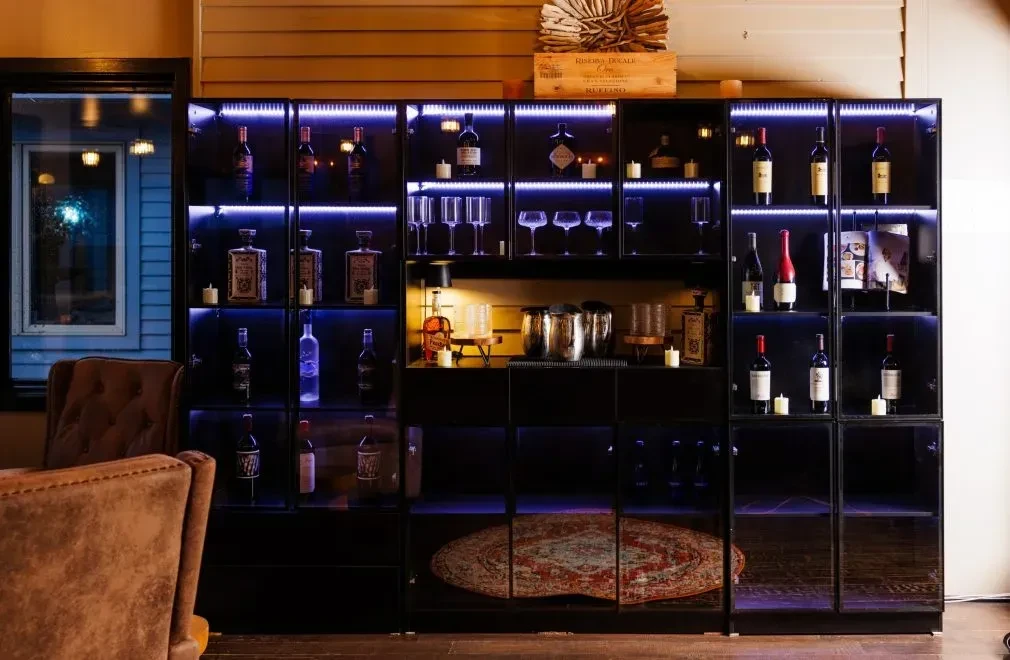 Dark bar cabinet with illuminated bottles, glassware, and candles.