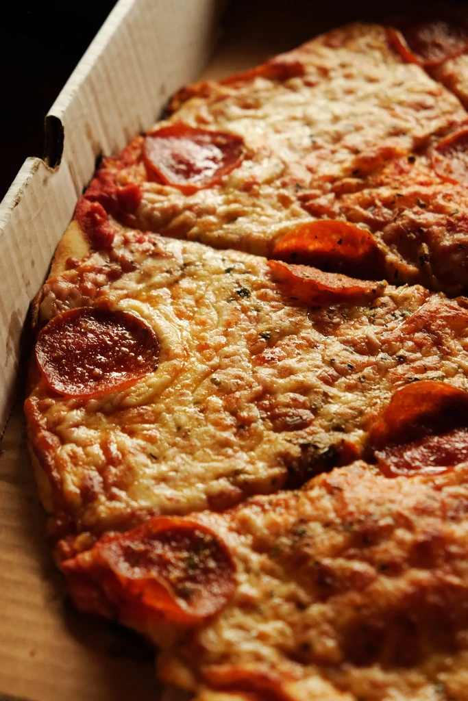 Pepperoni pizza with melted cheese and herbs in a cardboard box.