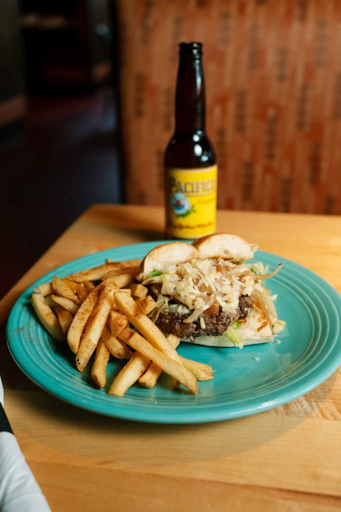 Half burger, french fries, and Pacifico beer bottle on wooden table.