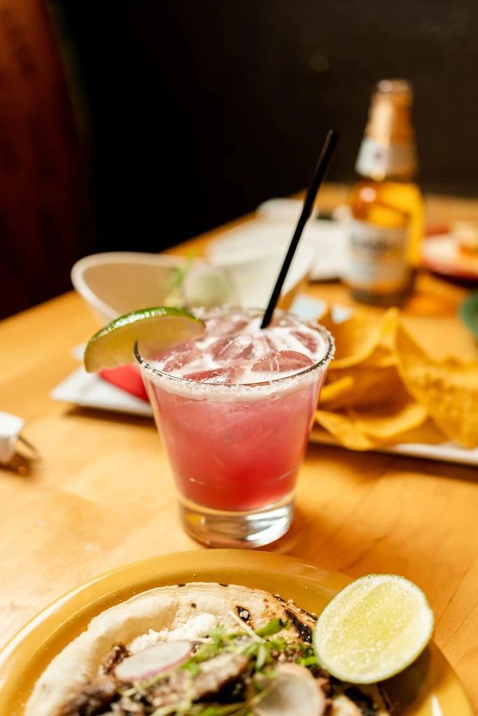 Pink margarita, taco, and chips on a warm-lit restaurant table.