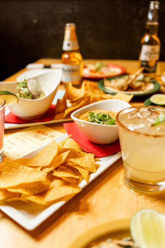 Restaurant table with chips, guacamole, cocktails, beer, and happy hour menu.